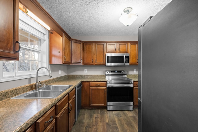 kitchen featuring dark wood-style flooring, appliances with stainless steel finishes, brown cabinetry, a sink, and a textured ceiling