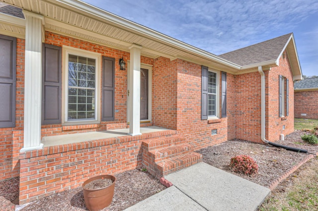 entrance to property with crawl space, brick siding, covered porch, and a shingled roof