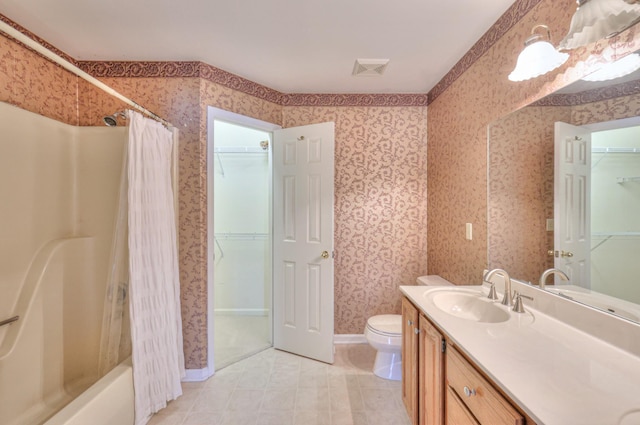 bathroom with vanity, baseboards, wallpapered walls, a walk in closet, and toilet