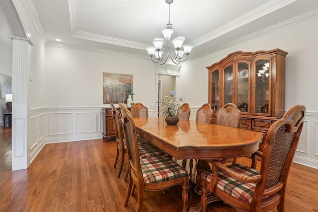 dining space featuring wood finished floors, an inviting chandelier, crown molding, a decorative wall, and ornate columns