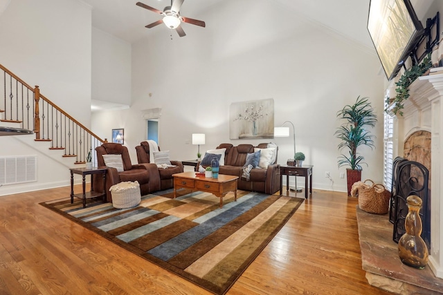 living room with visible vents, a fireplace with raised hearth, baseboards, stairway, and light wood-style floors