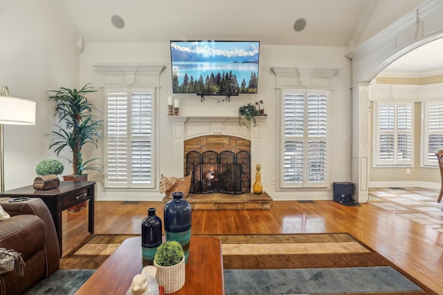 living room with wood finished floors, arched walkways, a fireplace, crown molding, and baseboards