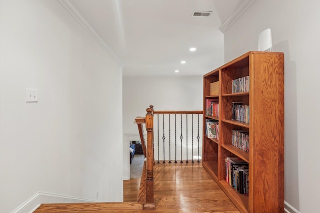 corridor with baseboards, wood finished floors, visible vents, and ornamental molding