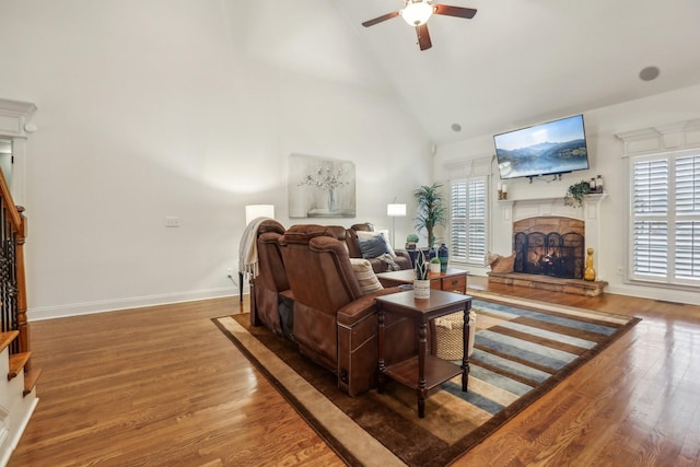 living room featuring ceiling fan, stairs, a stone fireplace, wood finished floors, and high vaulted ceiling