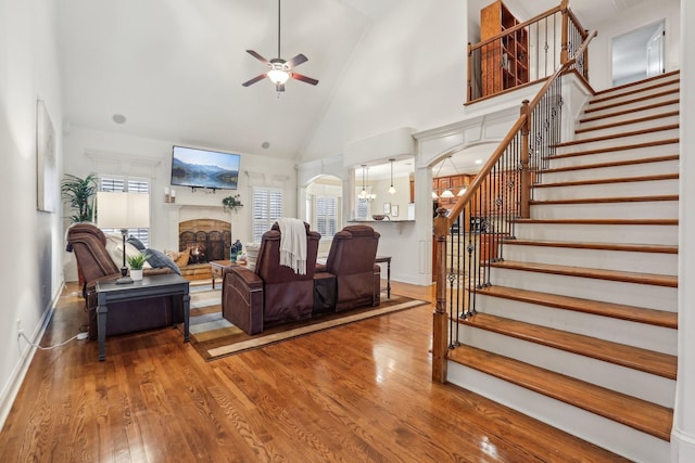 living area featuring a stone fireplace, stairs, wood finished floors, and arched walkways