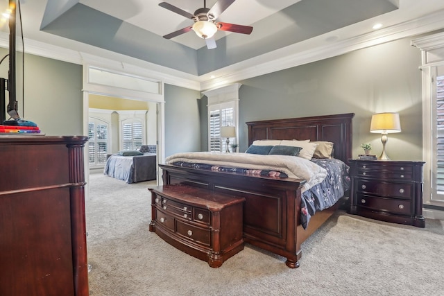 carpeted bedroom with a raised ceiling, ceiling fan, and ornamental molding