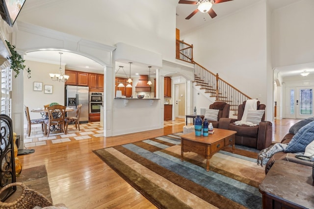 living room featuring ornamental molding, ceiling fan with notable chandelier, stairway, arched walkways, and light wood finished floors