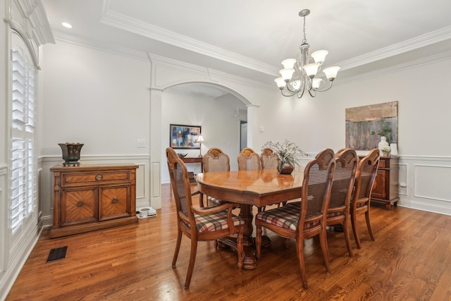 dining room with arched walkways, wood finished floors, ornamental molding, and a decorative wall