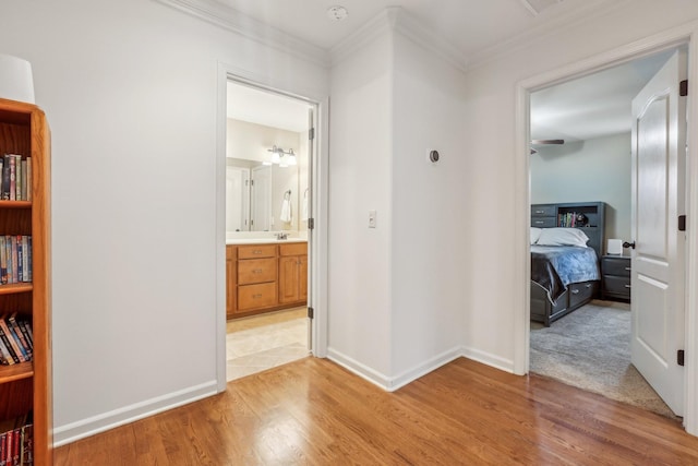 corridor with a sink, baseboards, light wood-style floors, and ornamental molding