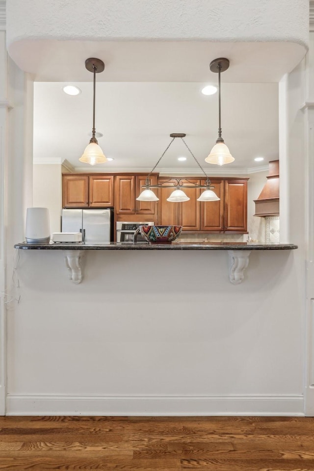 kitchen featuring hanging light fixtures, brown cabinets, freestanding refrigerator, and wood finished floors