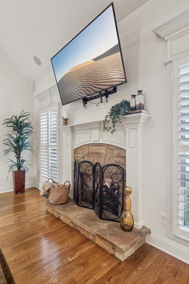 interior details with baseboards, a fireplace with raised hearth, wood finished floors, and crown molding