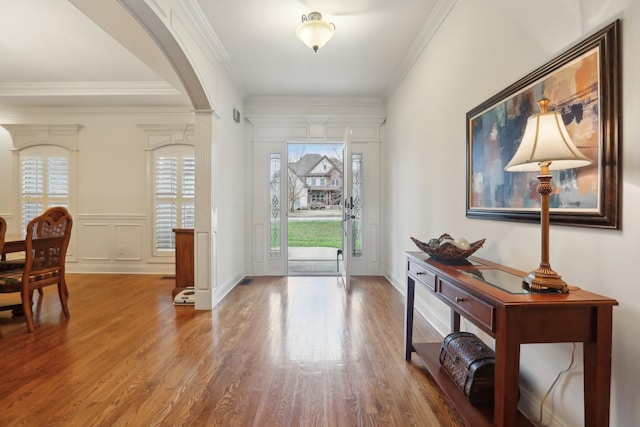 foyer entrance featuring crown molding, a decorative wall, wood finished floors, and arched walkways