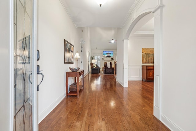 foyer entrance featuring a ceiling fan, wood finished floors, a fireplace, arched walkways, and crown molding