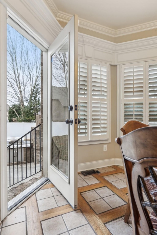 doorway to outside featuring tile patterned floors, baseboards, a healthy amount of sunlight, and crown molding