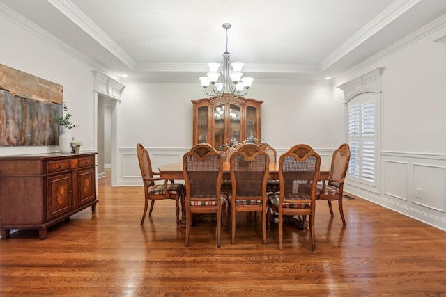 dining room with a notable chandelier, wood finished floors, crown molding, and a decorative wall