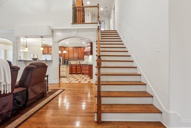 stairway with arched walkways, ornamental molding, a high ceiling, and wood finished floors