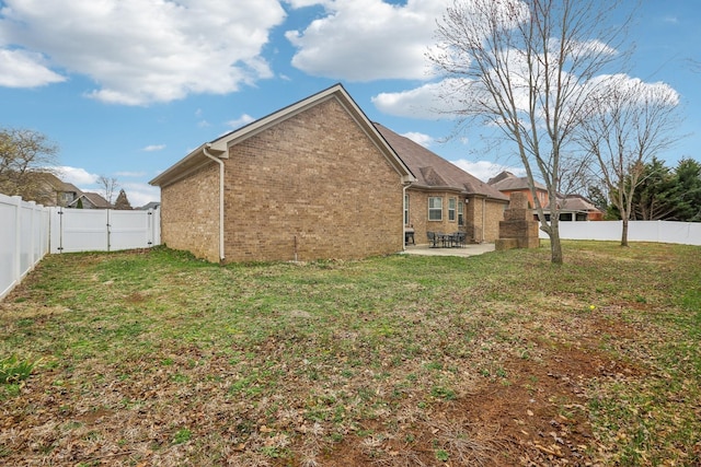 back of house with a gate, a patio, a fenced backyard, a yard, and brick siding