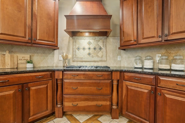 kitchen with dark stone countertops, custom range hood, light tile patterned flooring, and stainless steel gas cooktop