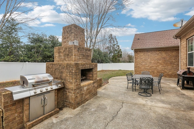 view of patio / terrace featuring an outdoor brick fireplace, fence, exterior kitchen, outdoor dining area, and a grill