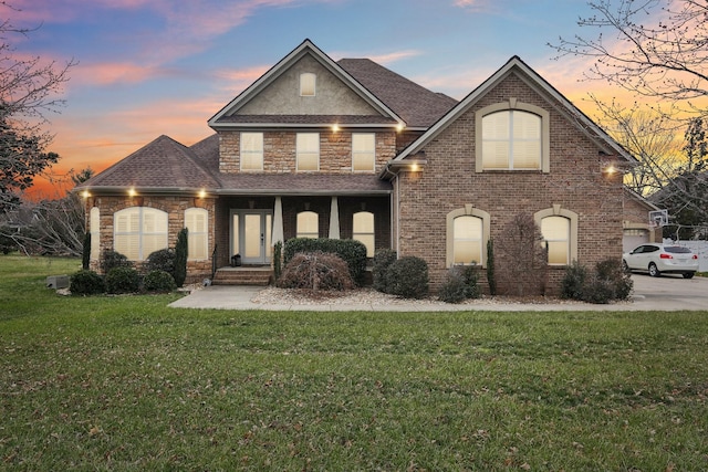 view of front facade featuring brick siding, roof with shingles, a front yard, stone siding, and driveway