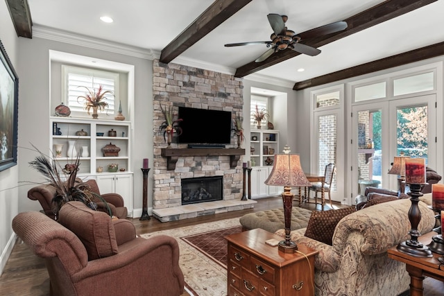 living area featuring ceiling fan, wood finished floors, crown molding, a stone fireplace, and beam ceiling