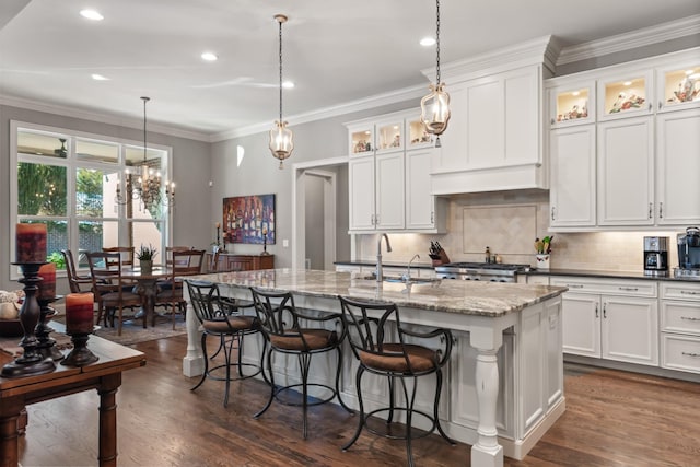 kitchen featuring a sink, decorative backsplash, an island with sink, dark wood finished floors, and crown molding