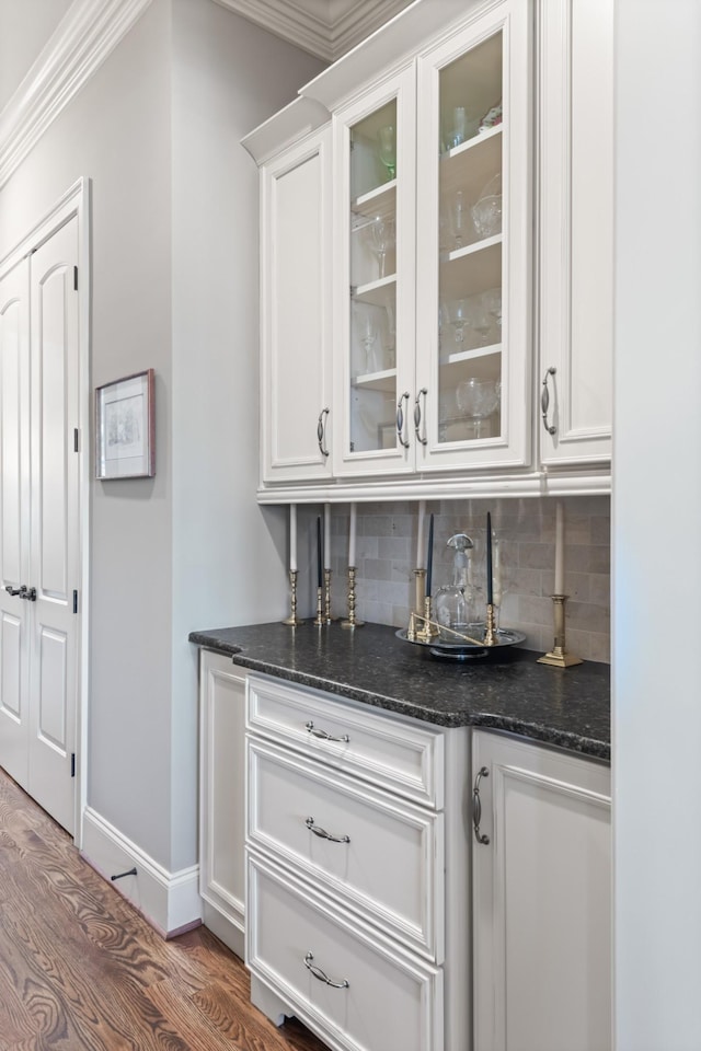 bar with baseboards, ornamental molding, backsplash, and wood finished floors