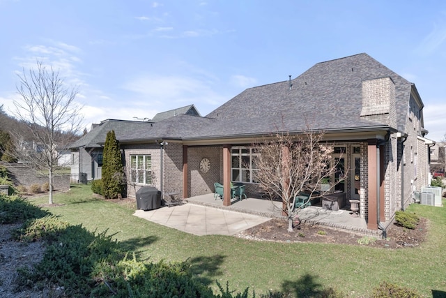 back of property with brick siding, roof with shingles, a lawn, and a patio