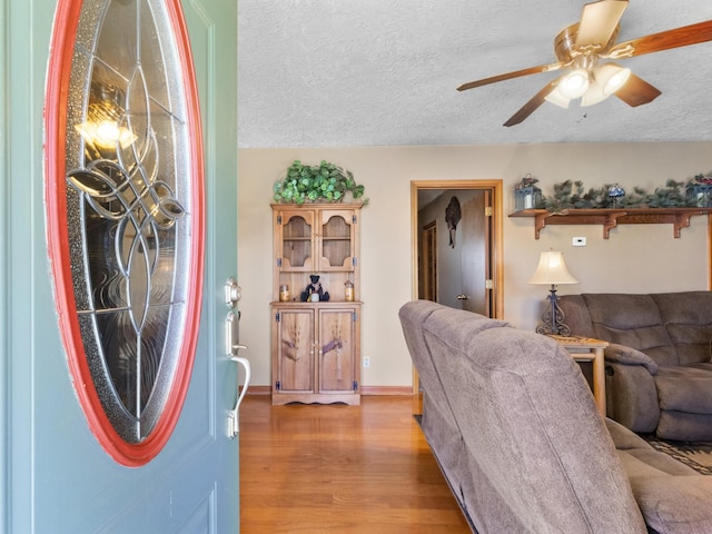 living room with light wood-type flooring, ceiling fan, baseboards, and a textured ceiling