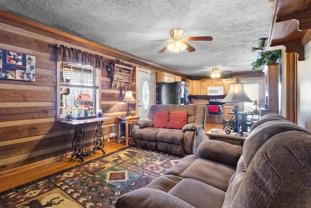 living room featuring a textured ceiling, wooden walls, a ceiling fan, and light wood-style floors