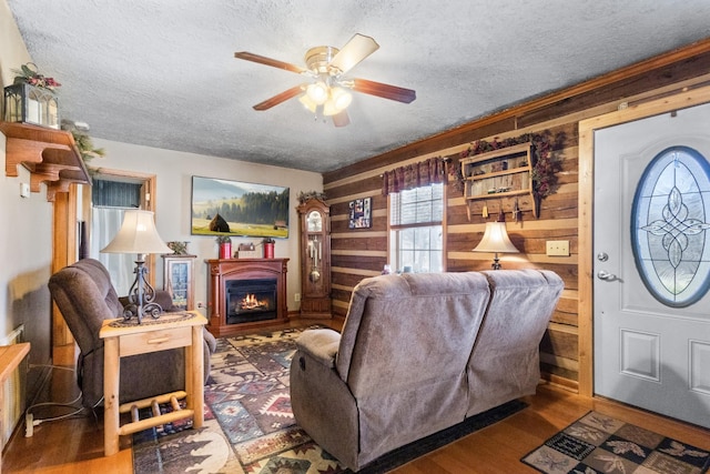 living room featuring a warm lit fireplace, wood walls, a textured ceiling, and wood finished floors