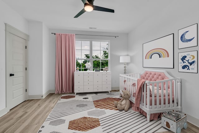 bedroom with visible vents, ceiling fan, wood finished floors, a crib, and baseboards