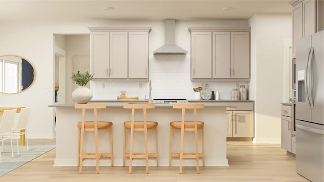 kitchen featuring wall chimney range hood, stainless steel refrigerator with ice dispenser, gray cabinets, decorative backsplash, and a center island with sink