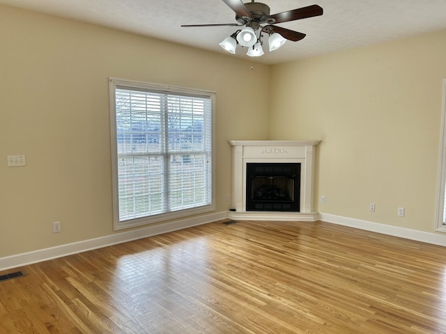 unfurnished living room featuring a fireplace with raised hearth, light wood-style flooring, a ceiling fan, visible vents, and baseboards