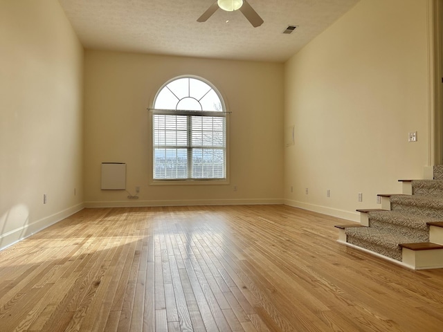 unfurnished room with visible vents, stairway, ceiling fan, light wood-type flooring, and baseboards