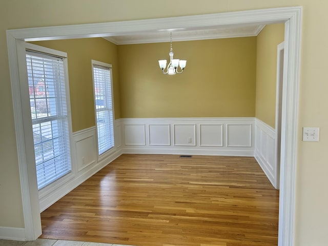 unfurnished room with ornamental molding, wainscoting, light wood-style flooring, and an inviting chandelier