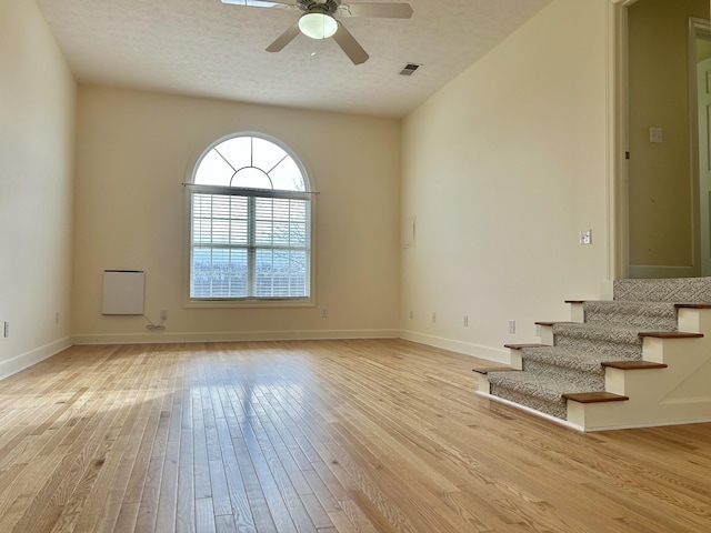 spare room featuring visible vents, light wood-style floors, a ceiling fan, baseboards, and stairs