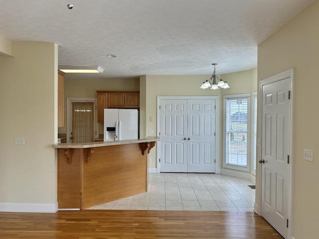 kitchen with a peninsula, a kitchen breakfast bar, light countertops, fridge with ice dispenser, and brown cabinetry