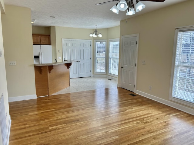 kitchen with a textured ceiling, a breakfast bar area, a peninsula, refrigerator with ice dispenser, and light wood finished floors