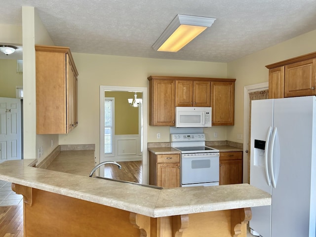 kitchen with a peninsula, white appliances, a kitchen bar, and brown cabinets