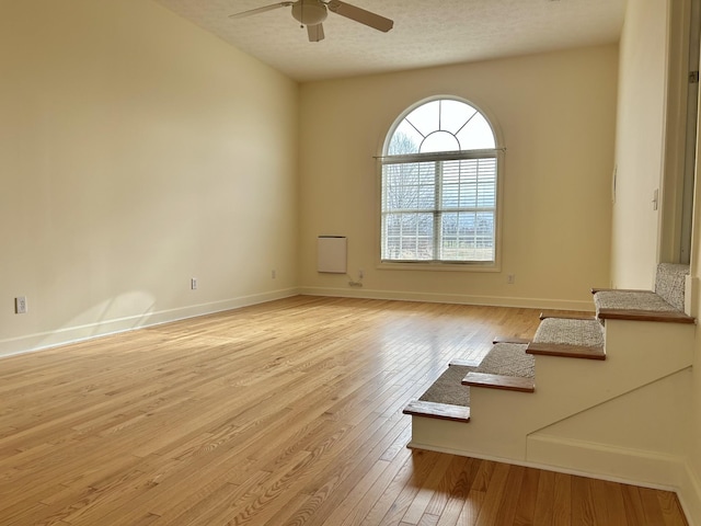 unfurnished room with light wood-type flooring, ceiling fan, baseboards, and a textured ceiling