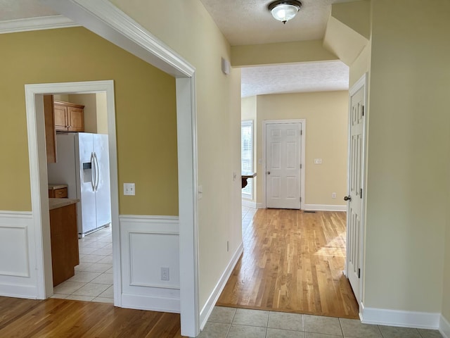 hall featuring light tile patterned floors, a textured ceiling, and wainscoting