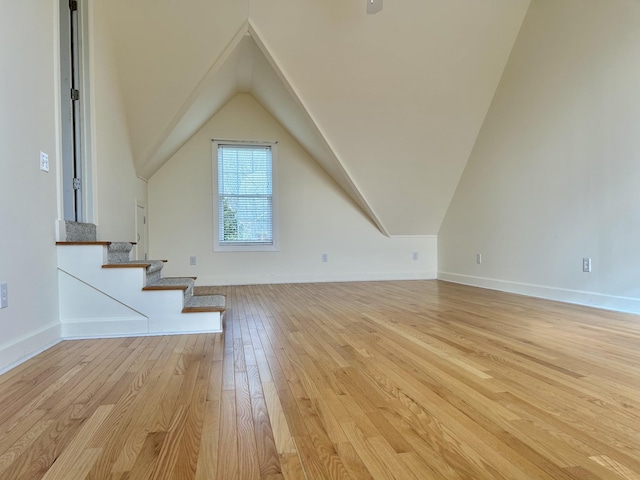 bonus room featuring light wood-style floors, baseboards, stairway, and vaulted ceiling