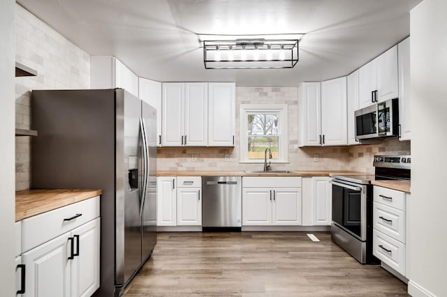 kitchen featuring stainless steel appliances, butcher block counters, a sink, white cabinets, and light wood finished floors