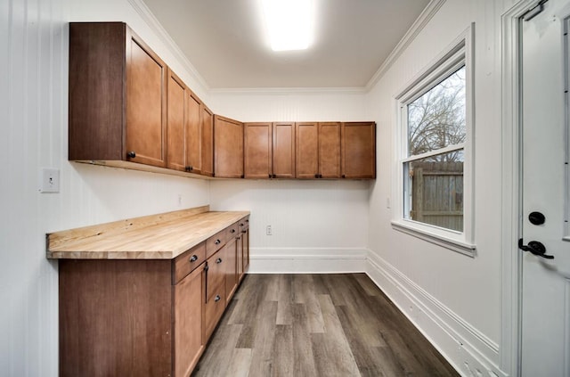 kitchen with dark wood-type flooring, brown cabinetry, ornamental molding, and baseboards