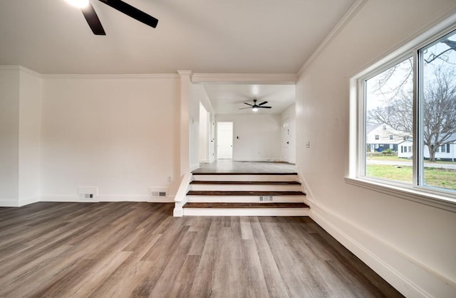 interior space with crown molding, visible vents, a ceiling fan, wood finished floors, and baseboards