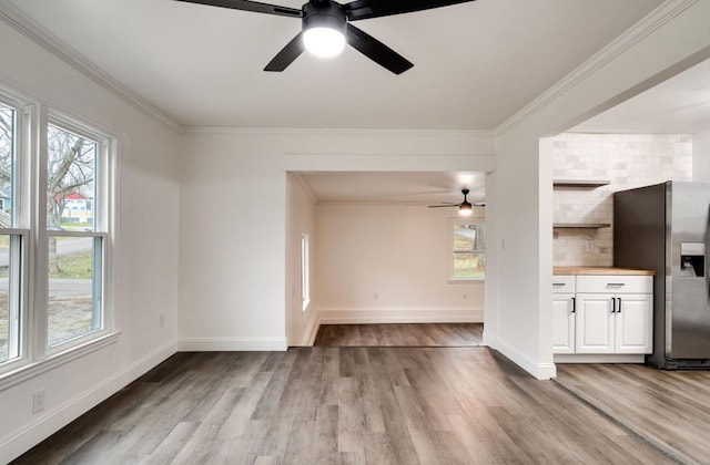 unfurnished living room featuring a healthy amount of sunlight, crown molding, baseboards, and wood finished floors