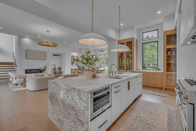 kitchen with a large island with sink, white cabinets, a sink, range with two ovens, and modern cabinets
