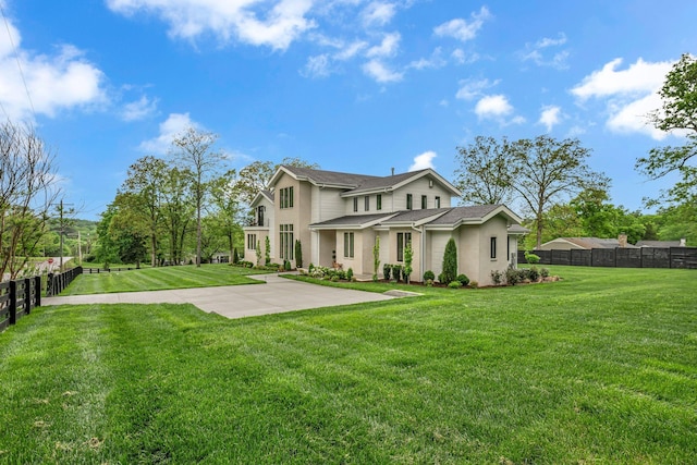 view of front facade featuring fence, stucco siding, a front yard, and roof with shingles
