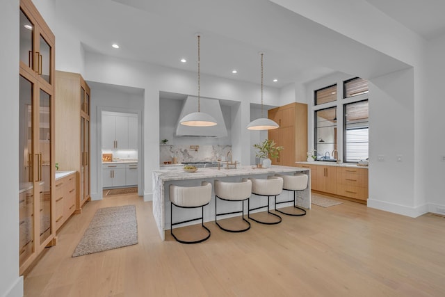 kitchen with a breakfast bar, premium range hood, light wood-style flooring, and backsplash